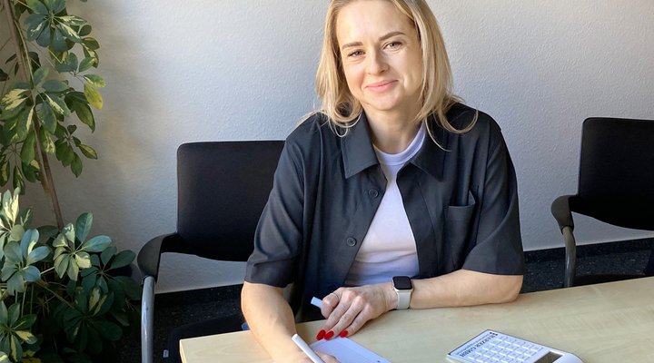Antonina Golovatiuktonya Eine Frau sitzt an einem Schreibtisch und hält einen Stift in der Hand