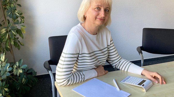 Liudmyla Maleniuk Eine Frau sitzt an einem Schreibtisch und blickt in die Kamera
