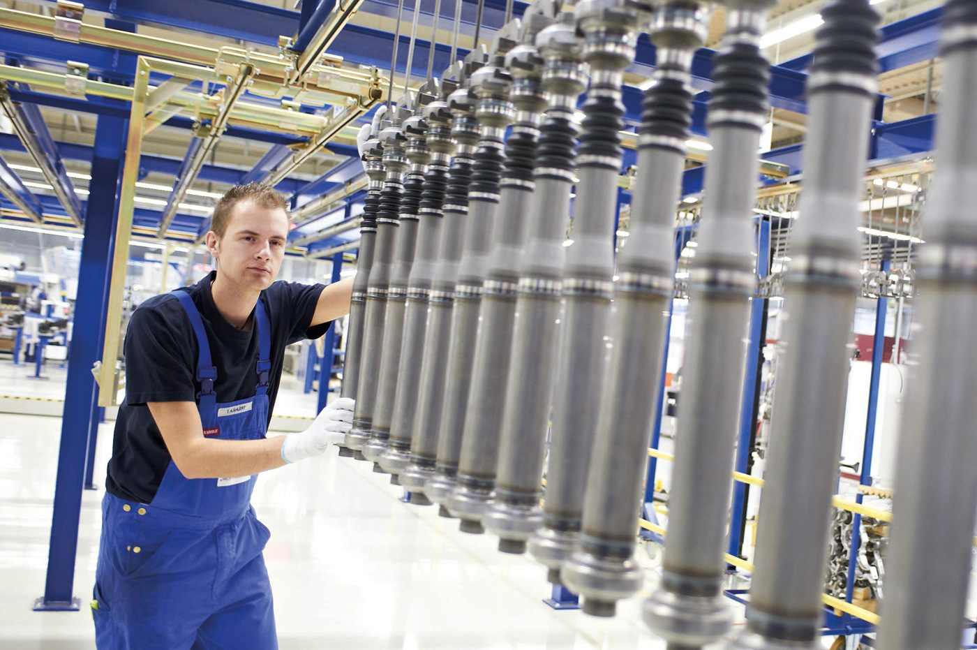 Ein Mann im Blaumann und weißen Handschuhen bedient eine Maschine in einer großen Produktionshalle